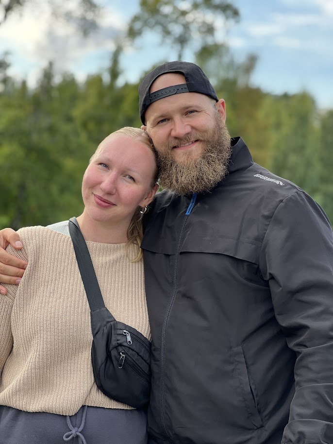 Katariina nojaa Joonaksen olkaan ulkona, taustalla puita ja pilvinen taivas